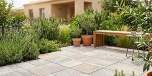 Pavimento de adoquín ecológico drenante en un patio residencial con plantas mediterráneas y mobiliario de madera. Solución sostenible para evitar charcos en el jardín en 2026.